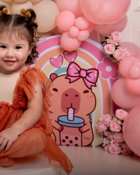 Niña con vestido naranja frente a un fondo de capibara rosado