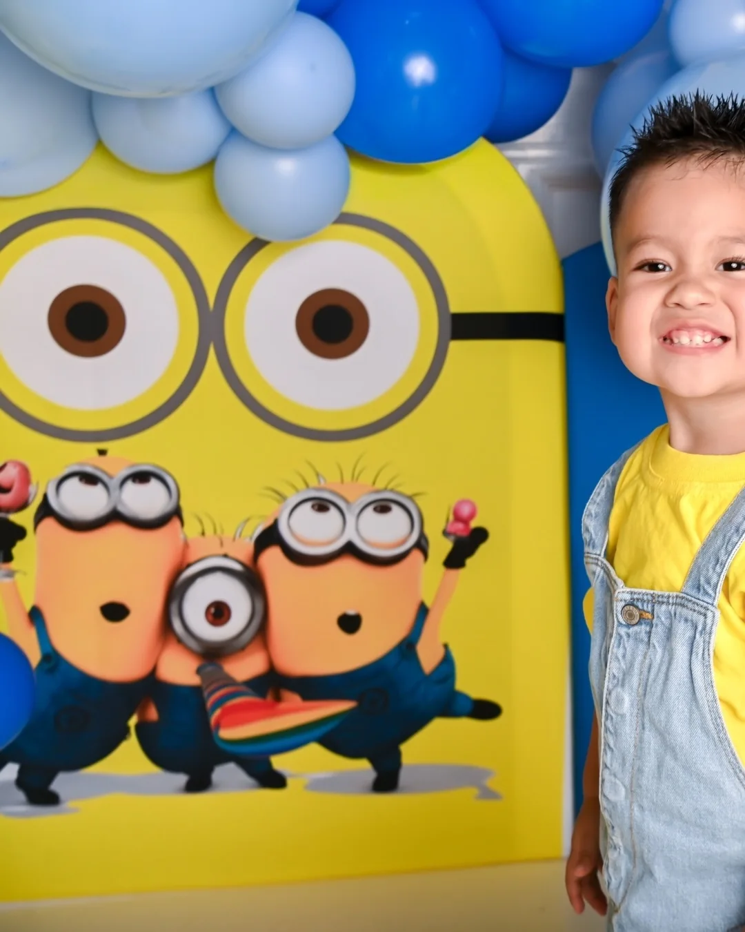 Niño sonriente en un set de Minions con globos azules y amarillos